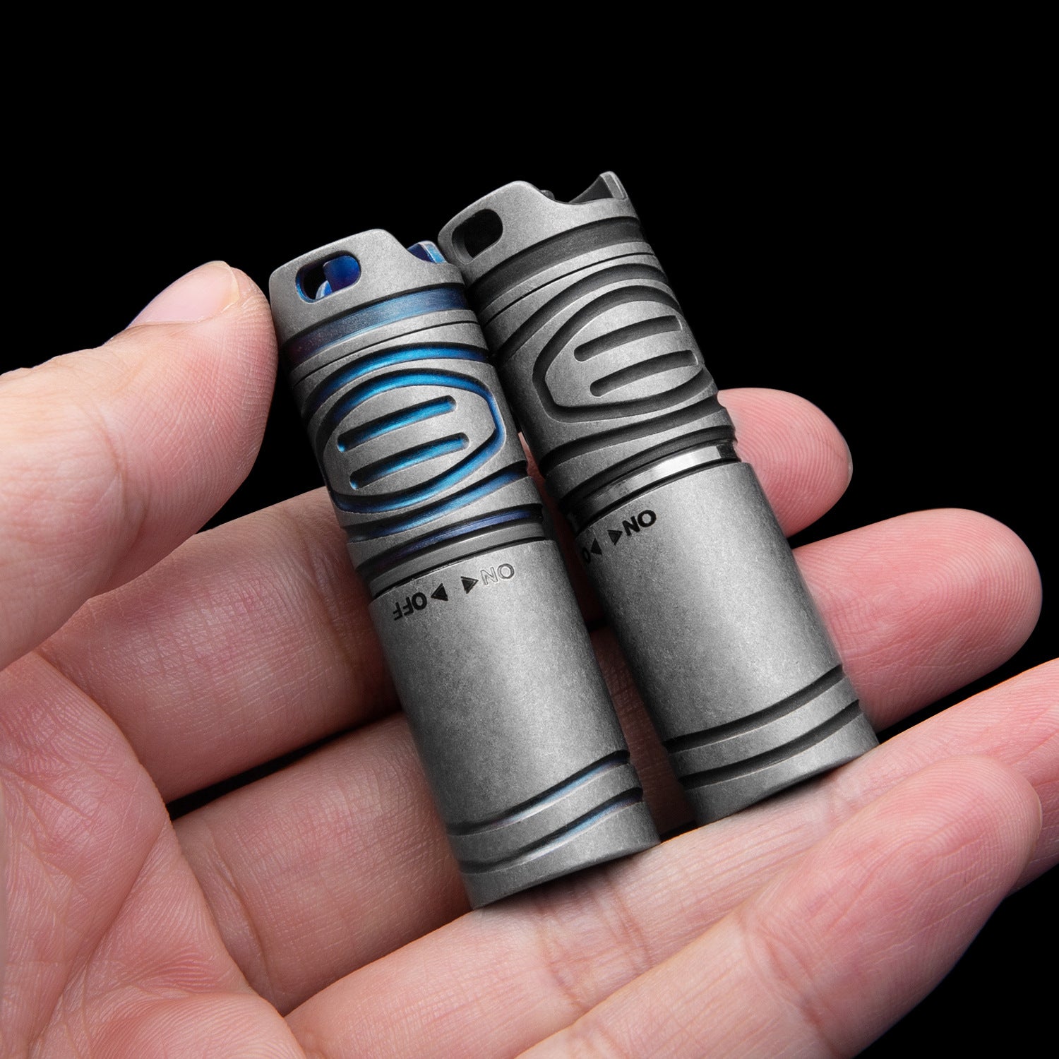 Two compact titanium alloy LED flashlights with blue accents, held in a person's hand.
