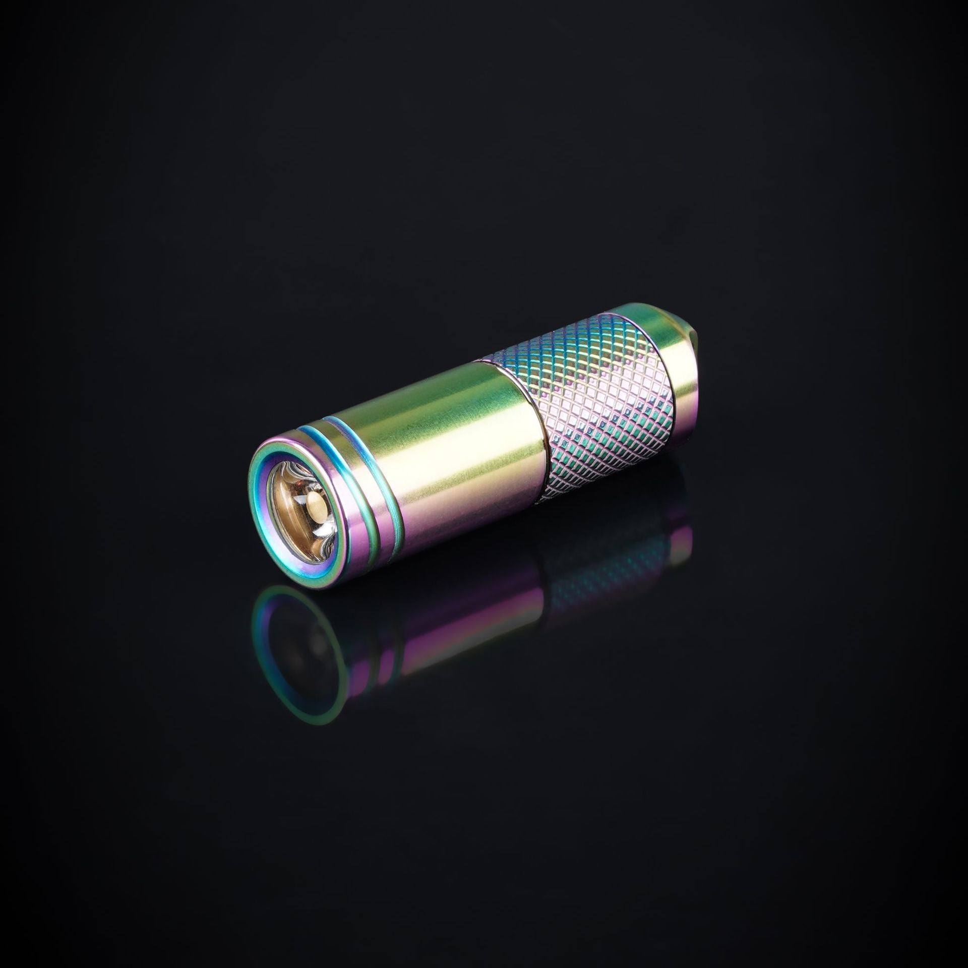 A titanium alloy mini flashlight with a multicolored rainbow coating, attached to a metal chain, displayed on a textured grey background.